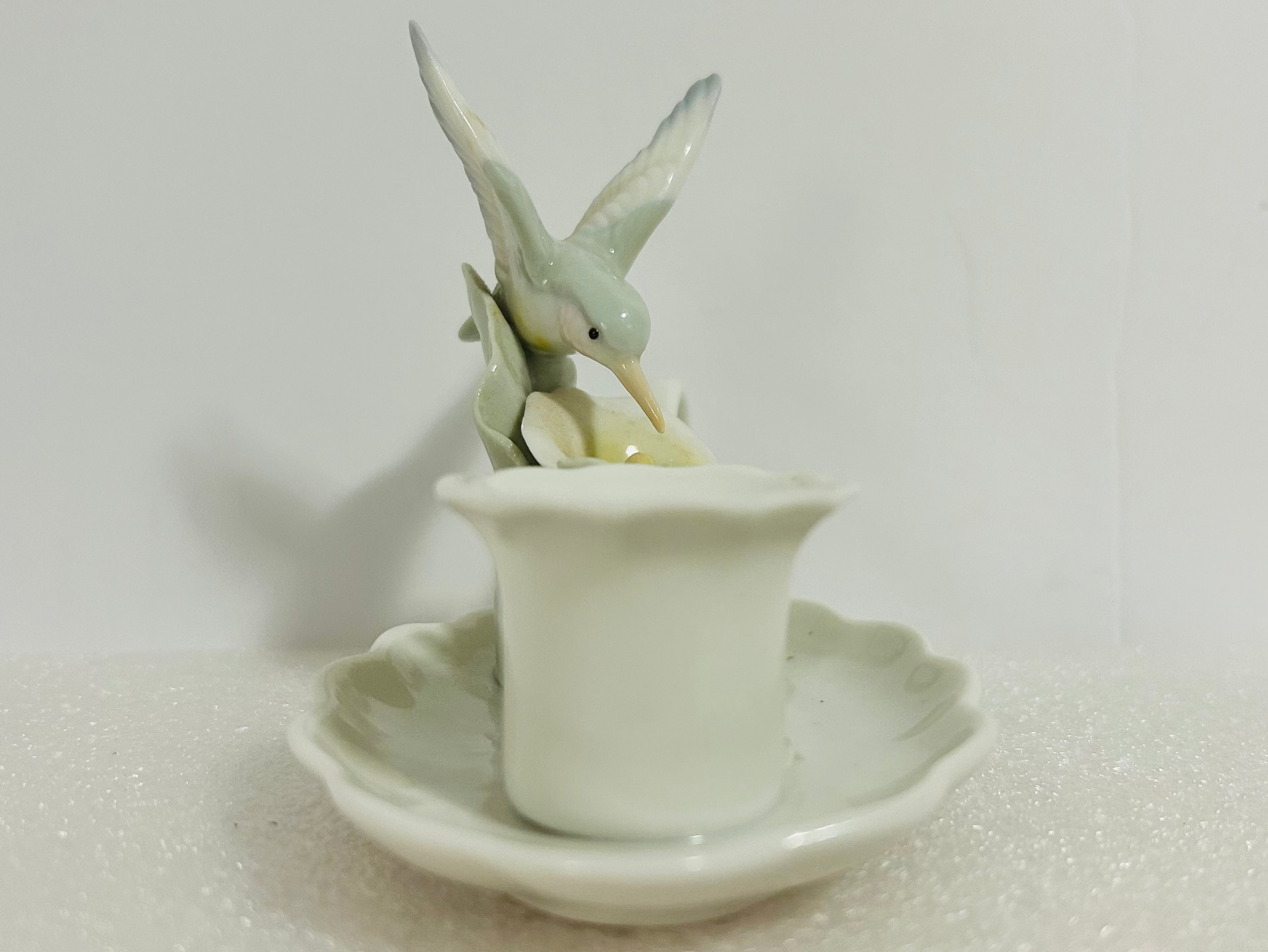 Small ceramic bird figurine on a white dish with a plain background
