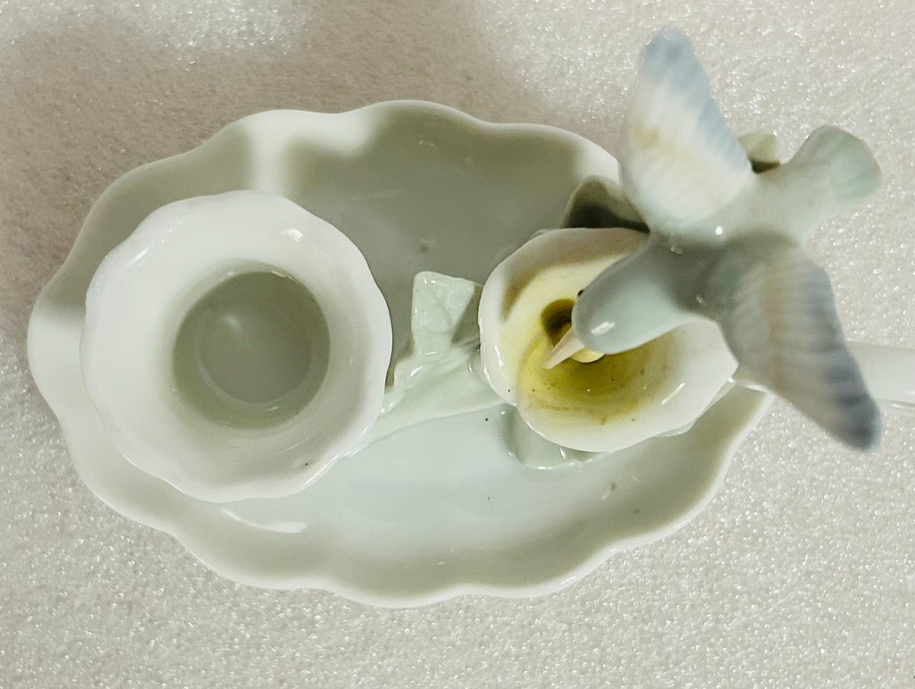 Small ceramic figurine of a bird on a leaf with a cup on a textured beige background