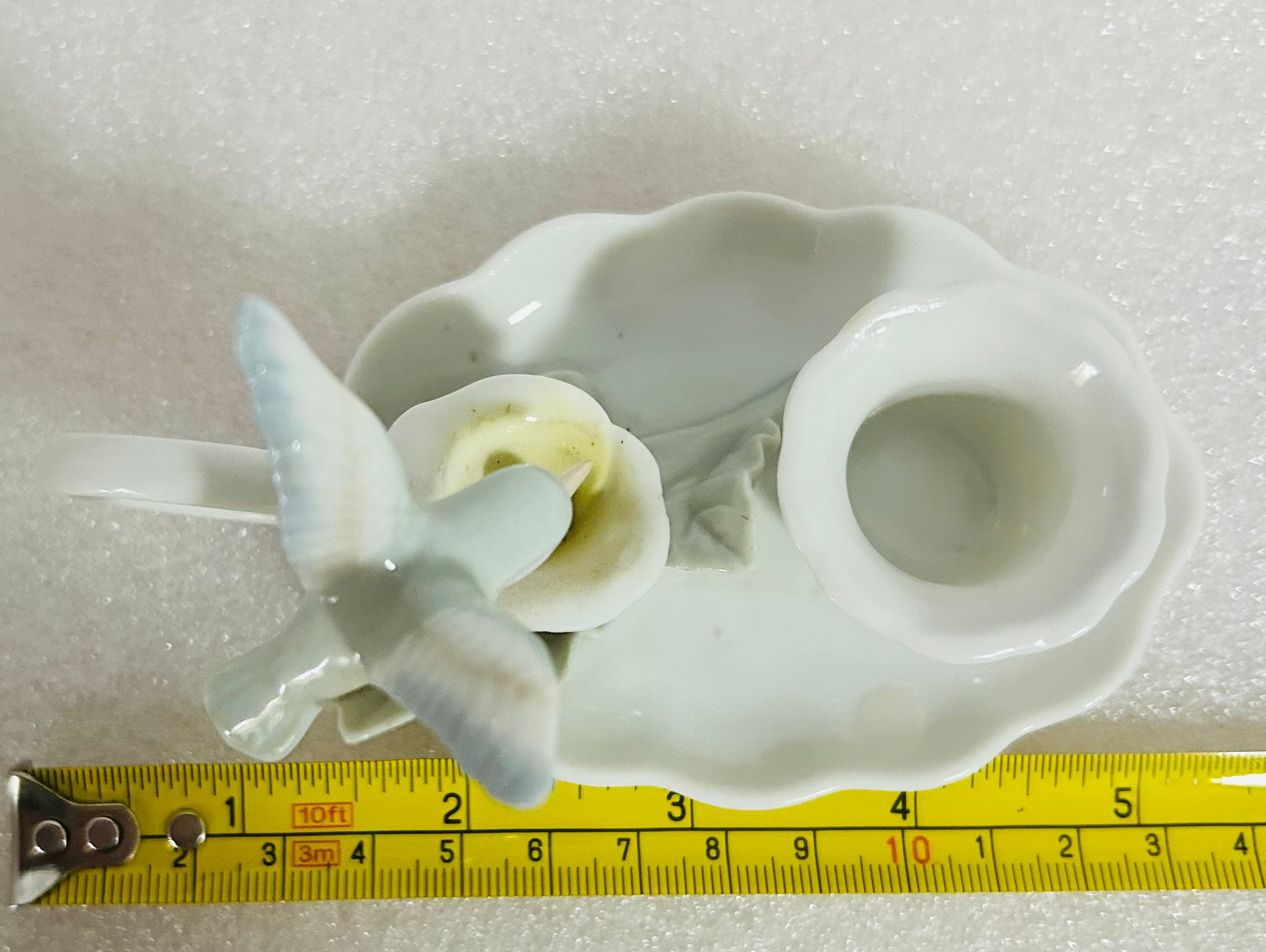 White ceramic shell with starfish on a white background, measured by a yellow ruler.