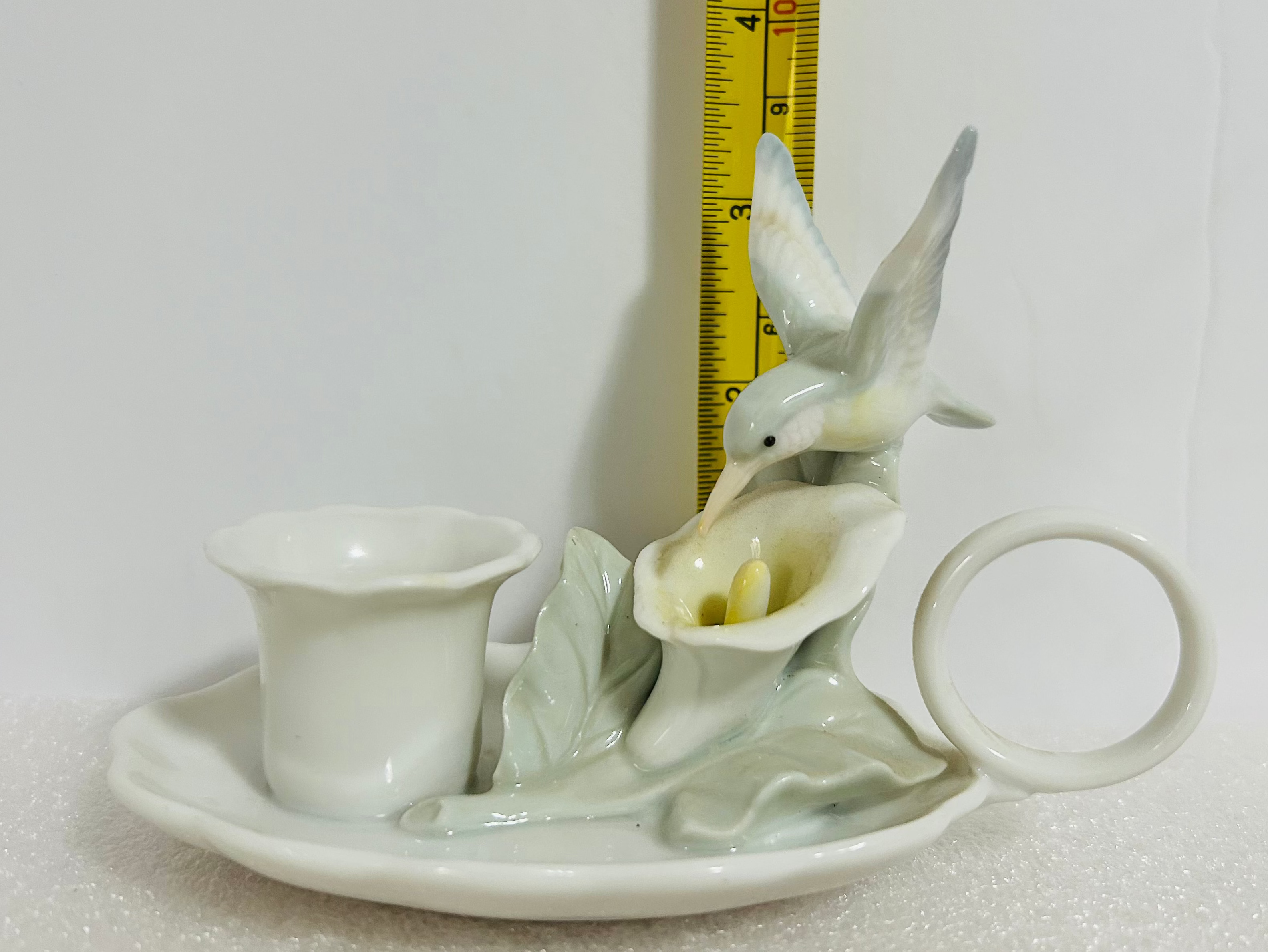 White ceramic teapot with lid and handle, placed on a white surface with a measuring tape for scale.